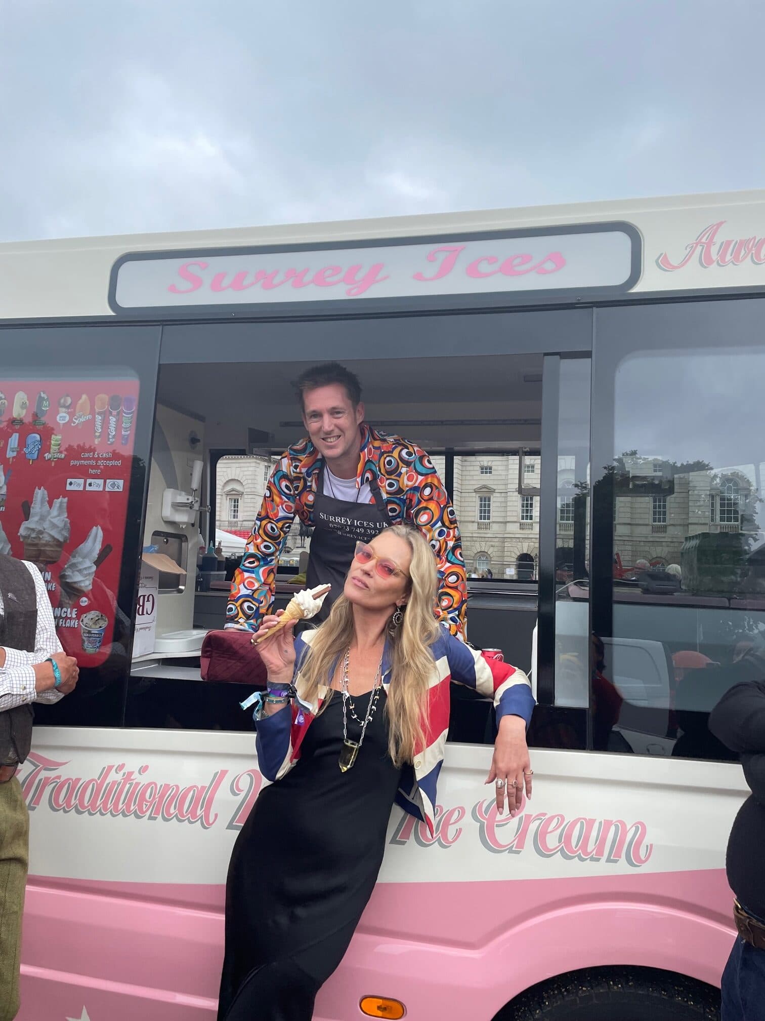 A woman in a Union Jack jacket holding a cone beside a cream and pink Hampshire Ices van
